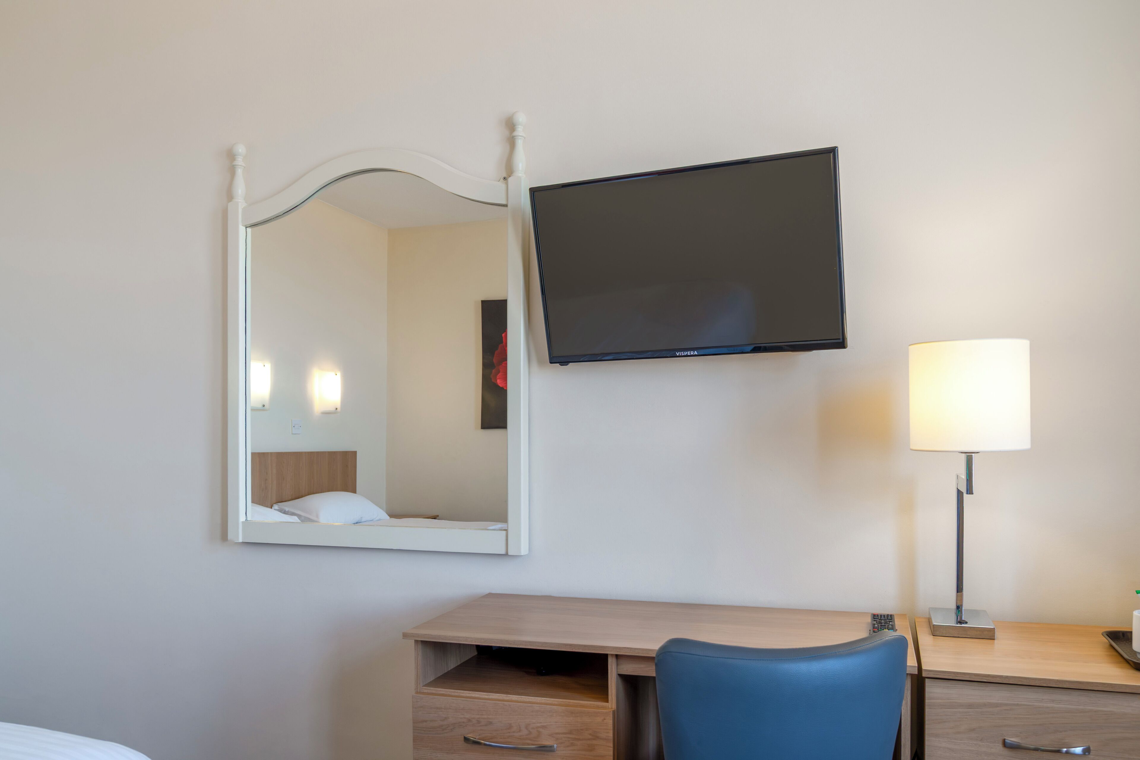 Een hotelkamer met een bed, een bureau met stoel, een flatscreen televisie, een bedlamp en een spiegel.