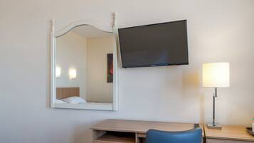 Een hotelkamer met een bed, een bureau met stoel, een flatscreen televisie, een bedlamp en een spiegel.