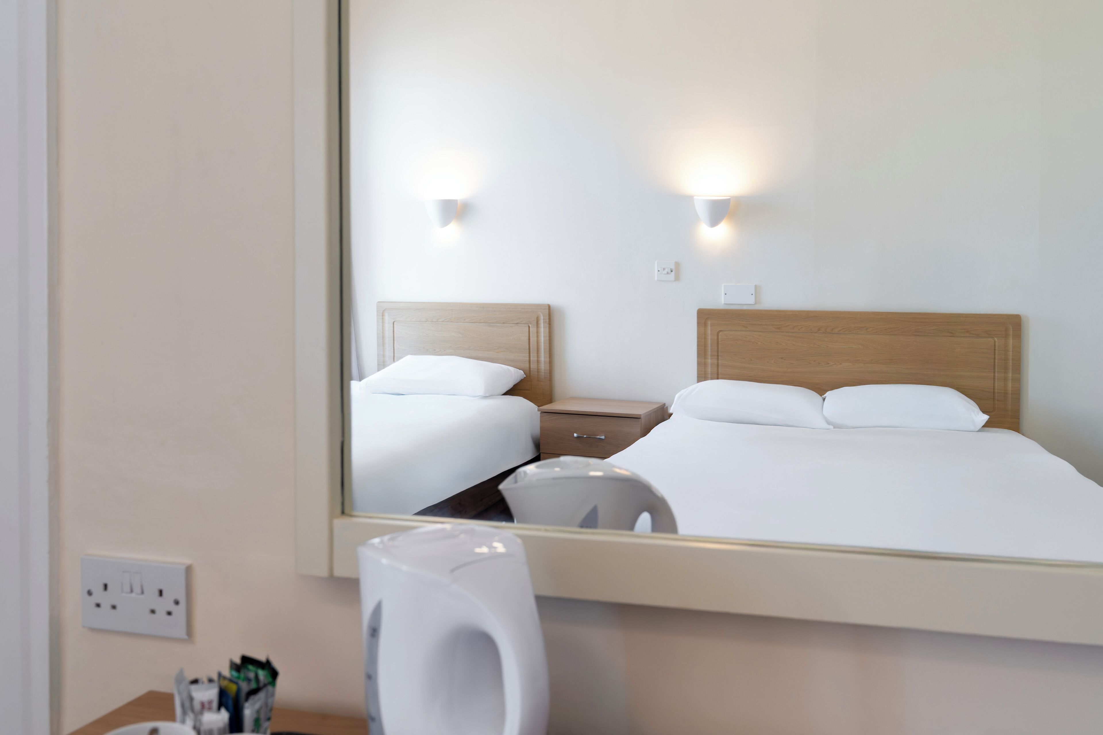 Hotellihuone, jossa on suuri peili, kaksi sänkyä, yöpöydät ja seinään kiinnitetyt valaisimet.