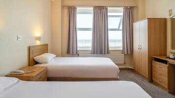 Een hotelkamer met twee bedden, een houten kledingkast, een bureau met lamp en een raam met gordijnen.