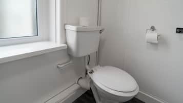A white toilet with a paper towel holder and a window above it.