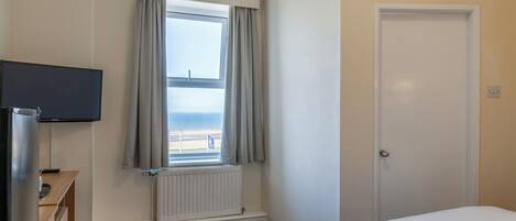 A hotel room with a bed, a television, a window with curtains, a radiator, and a door.