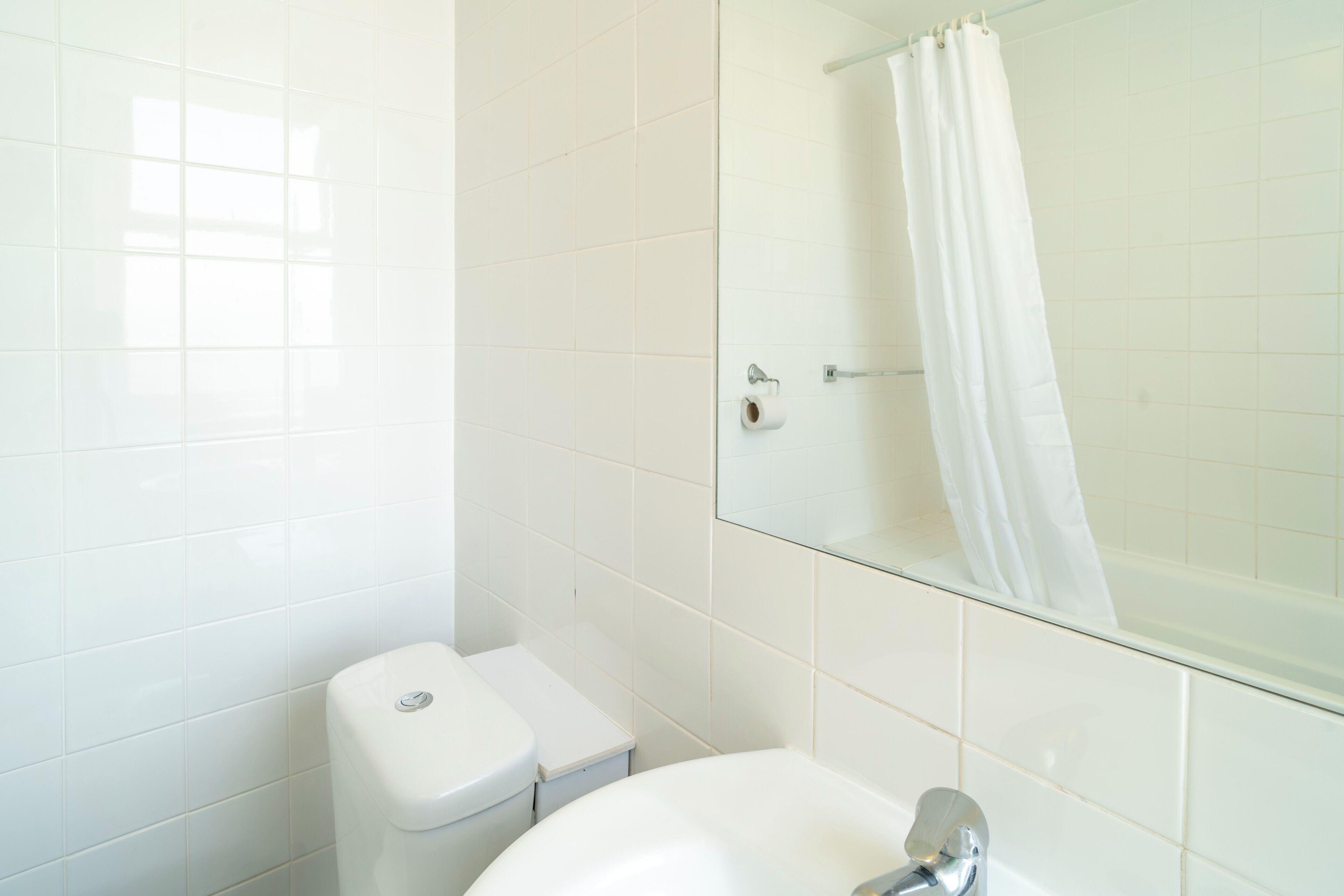 A bathroom with white tiles, a toilet, a sink, and a glass shower enclosure.