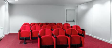 A conference room with rows of red chairs, white walls, and a carpeted floor.