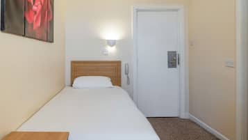 Una cama individual con cabecera de madera, una mesita de noche, una lámpara de pared y una puerta con cerradura.
