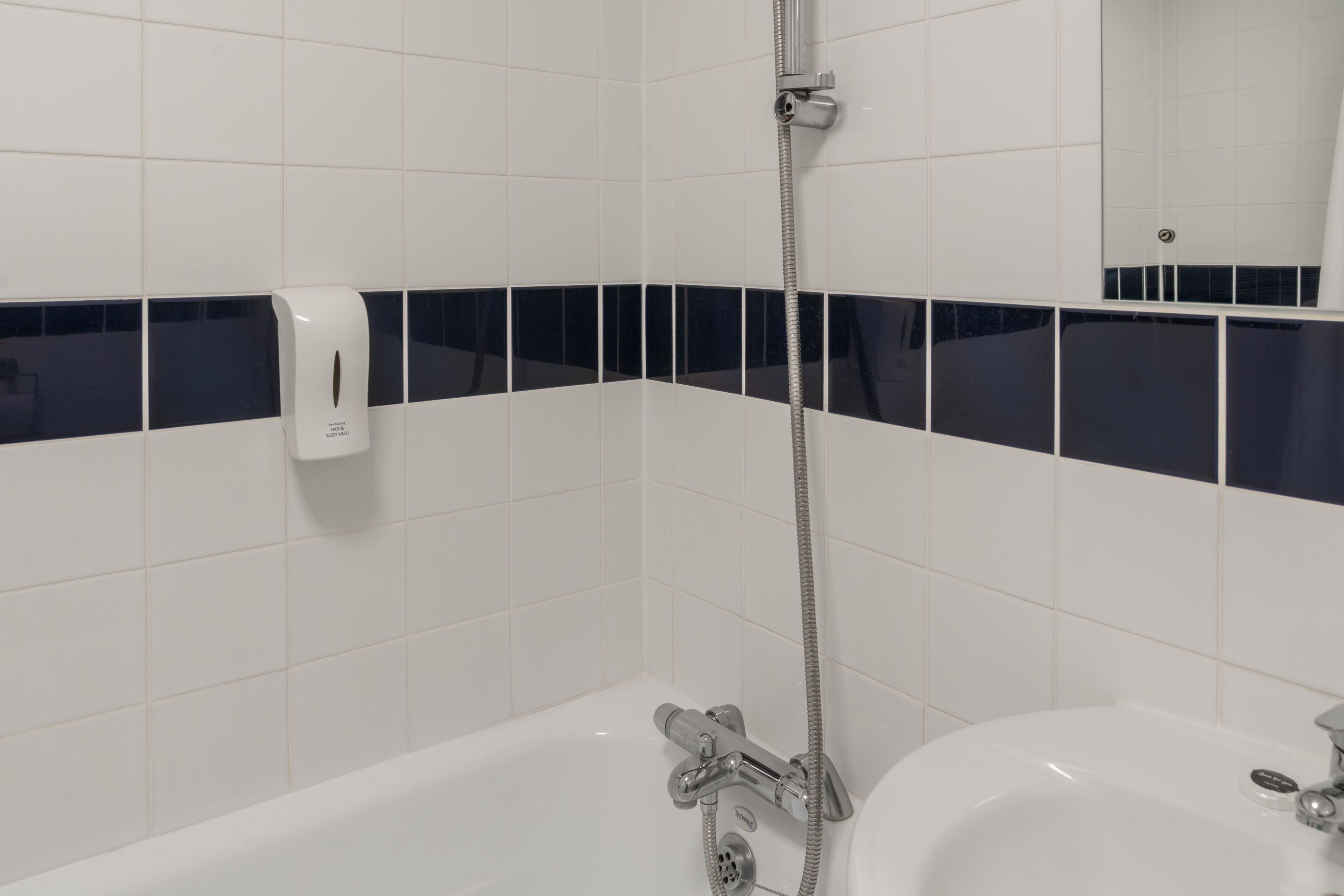 Een badkamer met witte tegels, een zwart accentstrookje, een handdouche en een zeepdispenser.