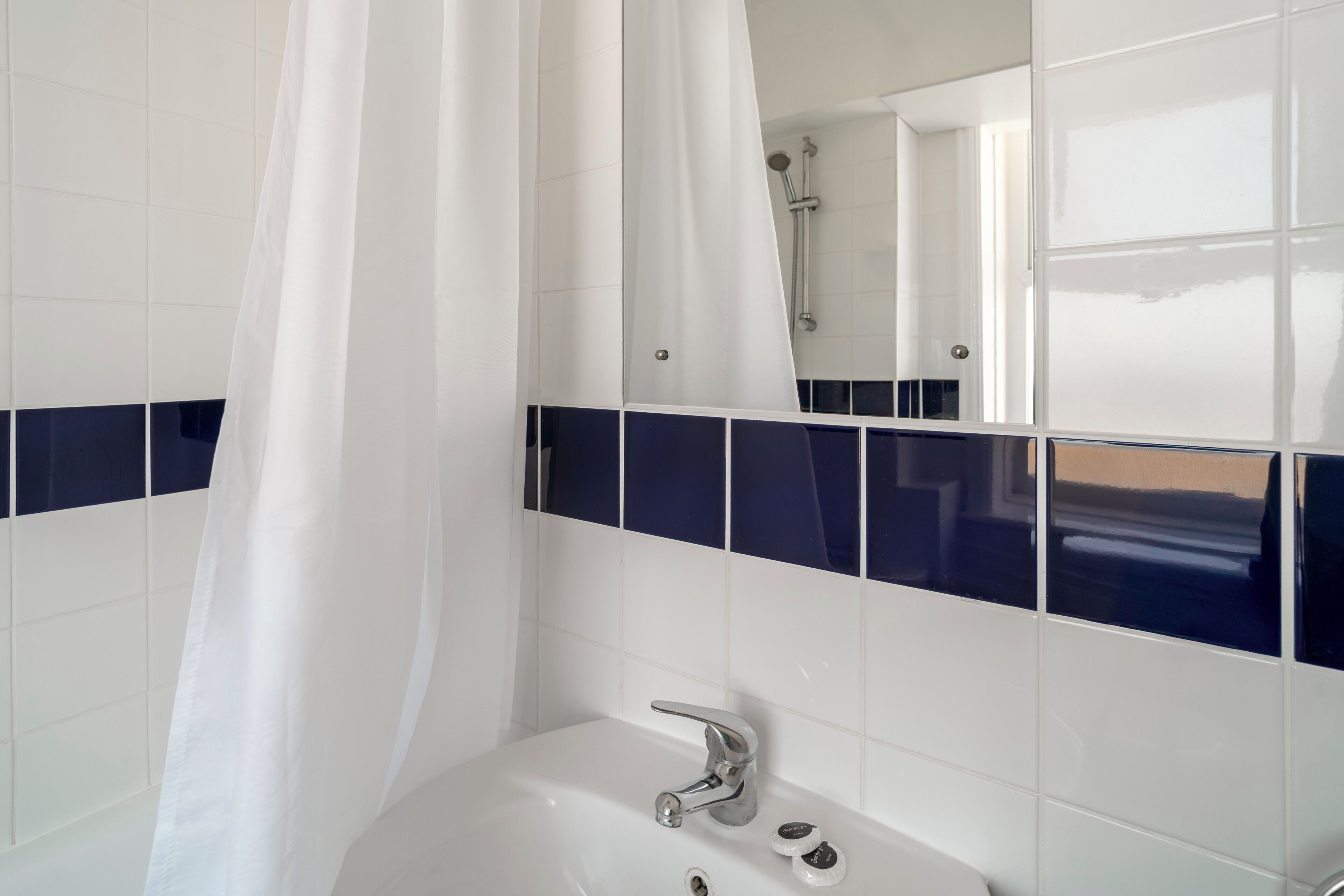Une salle de bain avec un lavabo blanc, une douche et un miroir.