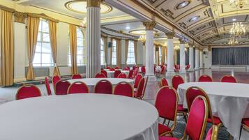 Een balzaal met ronde tafels, rode stoelen en gouden accenten.