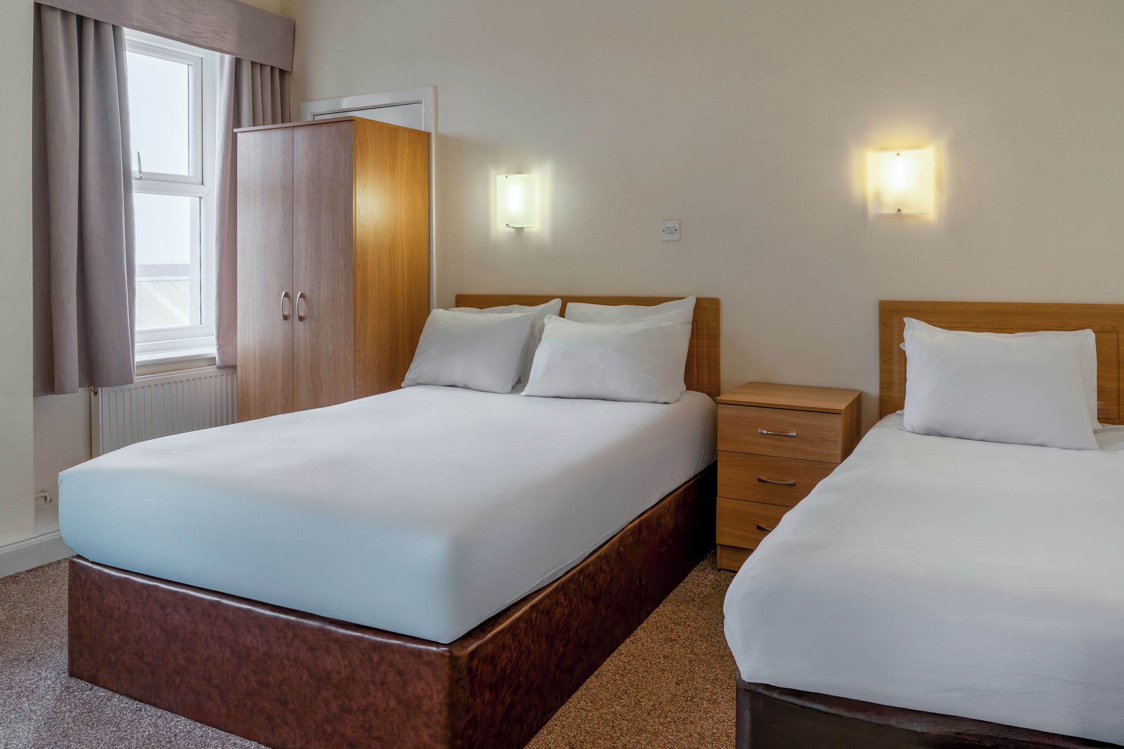 Habitación de hotel con una cama grande, un armario de madera, una mesita de noche y dos luces fijadas a la pared.