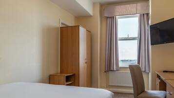 A hotel room with a bed, a wooden wardrobe, a desk with a chair, a television, and a window with curtains.