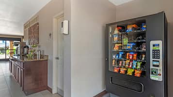Uma cozinha com máquina de vendas de lanches, cafeteira e geladeira.