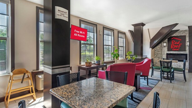 A modern hotel room with a breakfast area, a Red Roof Inn sign, and a view of the outdoors. - Red Roof Inn Gastonia (Gastonia)