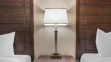 A hotel room with a bed, a nightstand with a lamp, and wooden paneling on the walls.