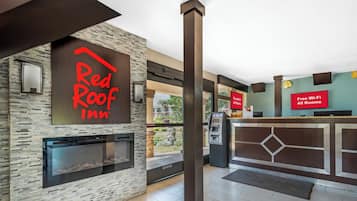Área de recepção do Red Roof Inn com parede de pedra, lareira, caixa eletrônico e aviso indicando Wi-Fi gratuito em todos os quartos.