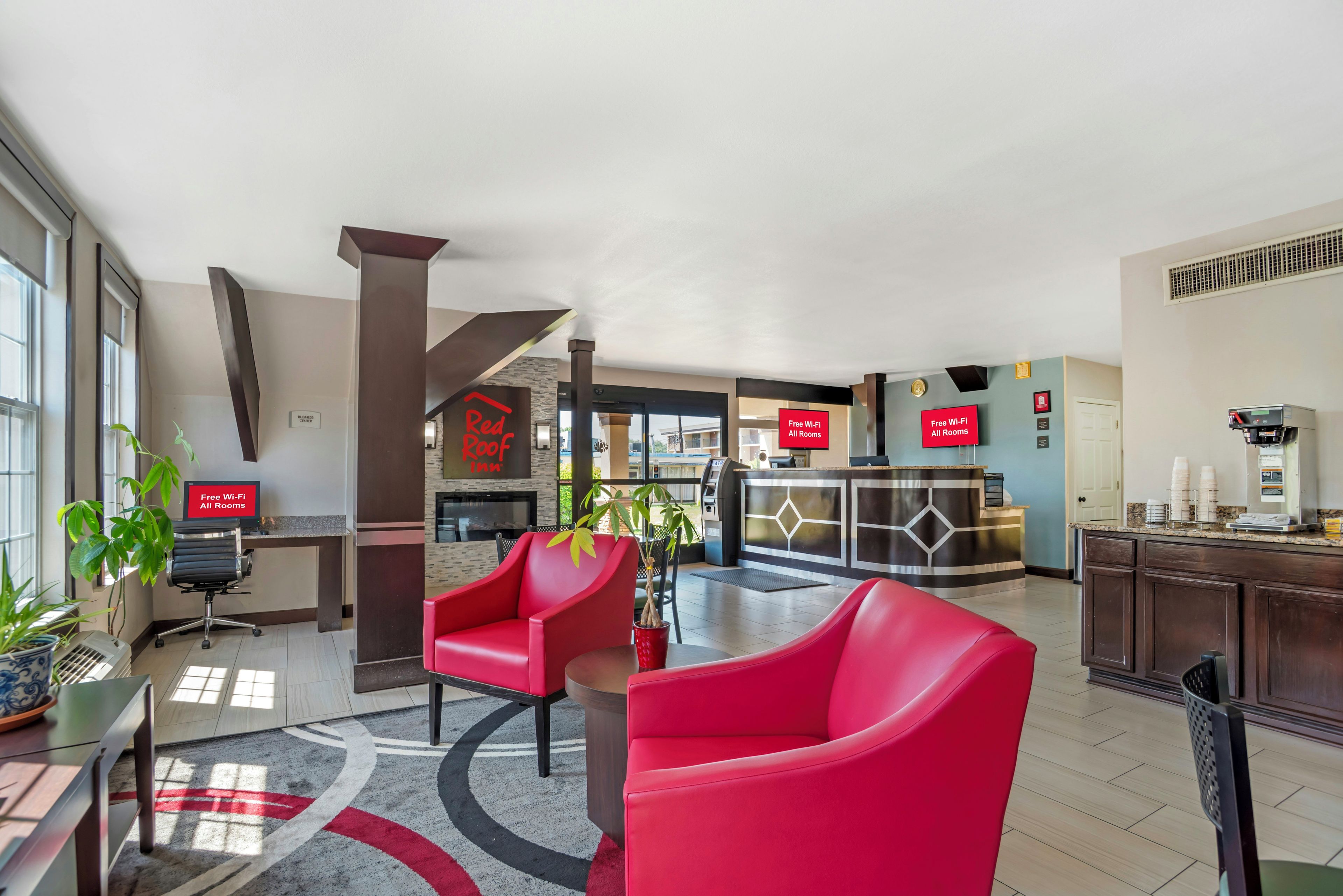 Un vestíbulo de hotel con sillas rojas, una recepción y una zona de cocina.