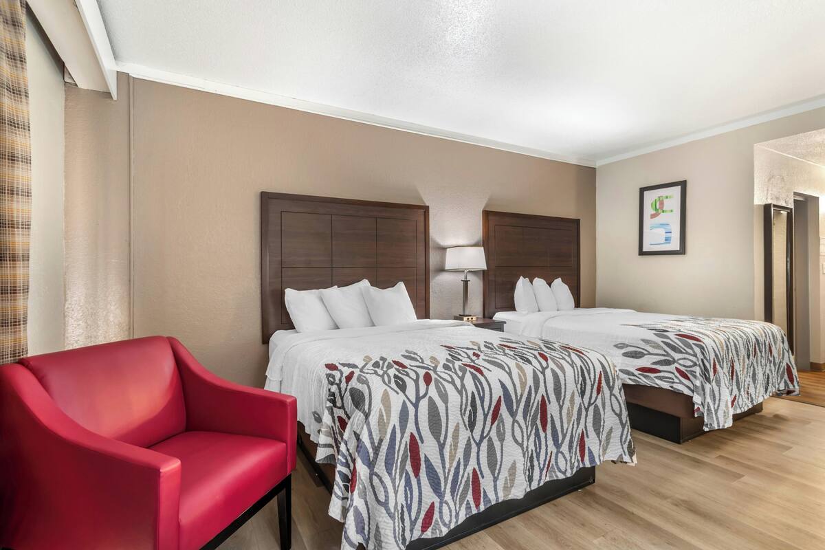 Ein Hotelzimmer mit zwei Betten, einem roten Sessel, einer Lampe und einem gerahmten Bild an der Wand.