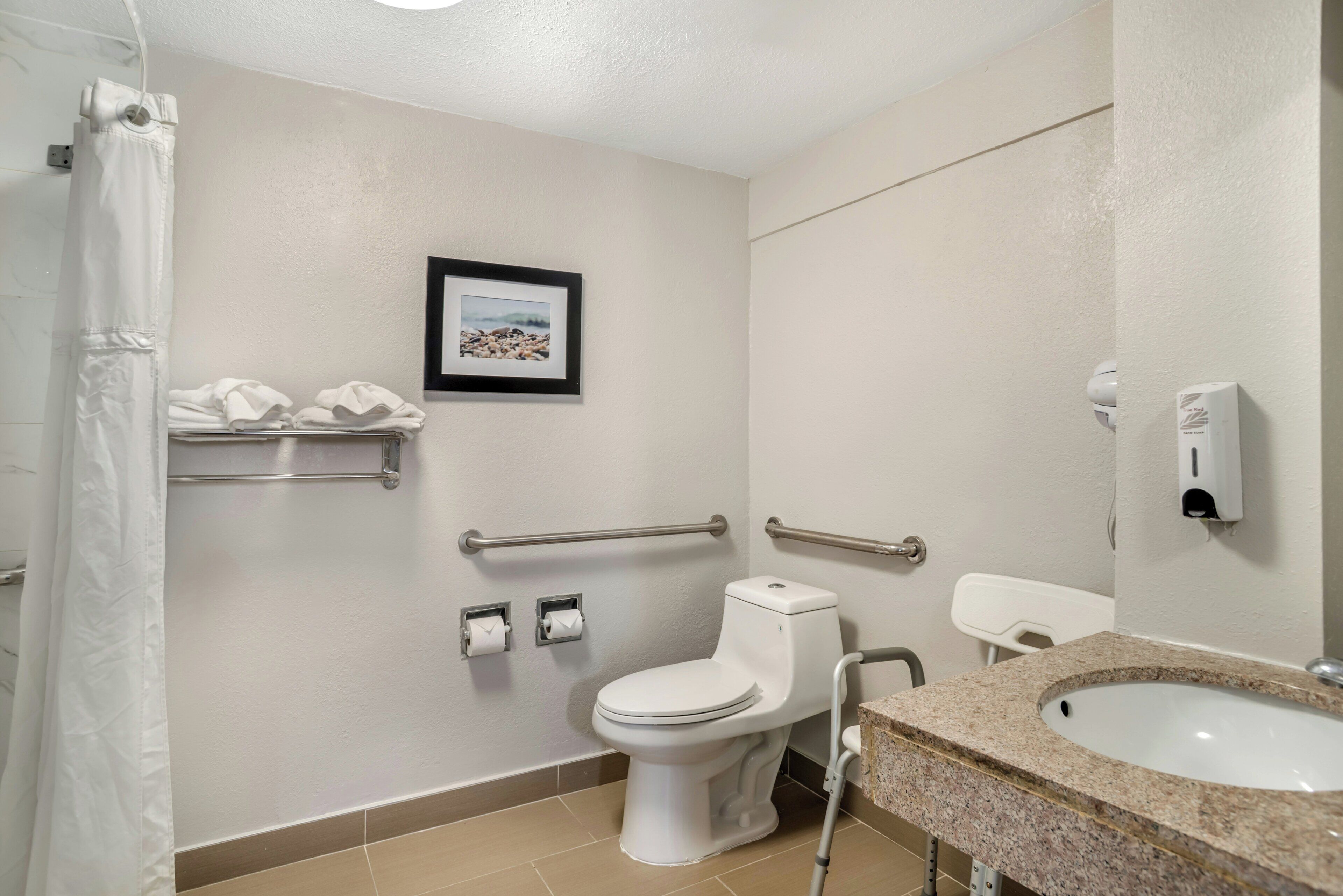 Un baño con inodoro, barras de apoyo, lavabo y cortina de ducha.