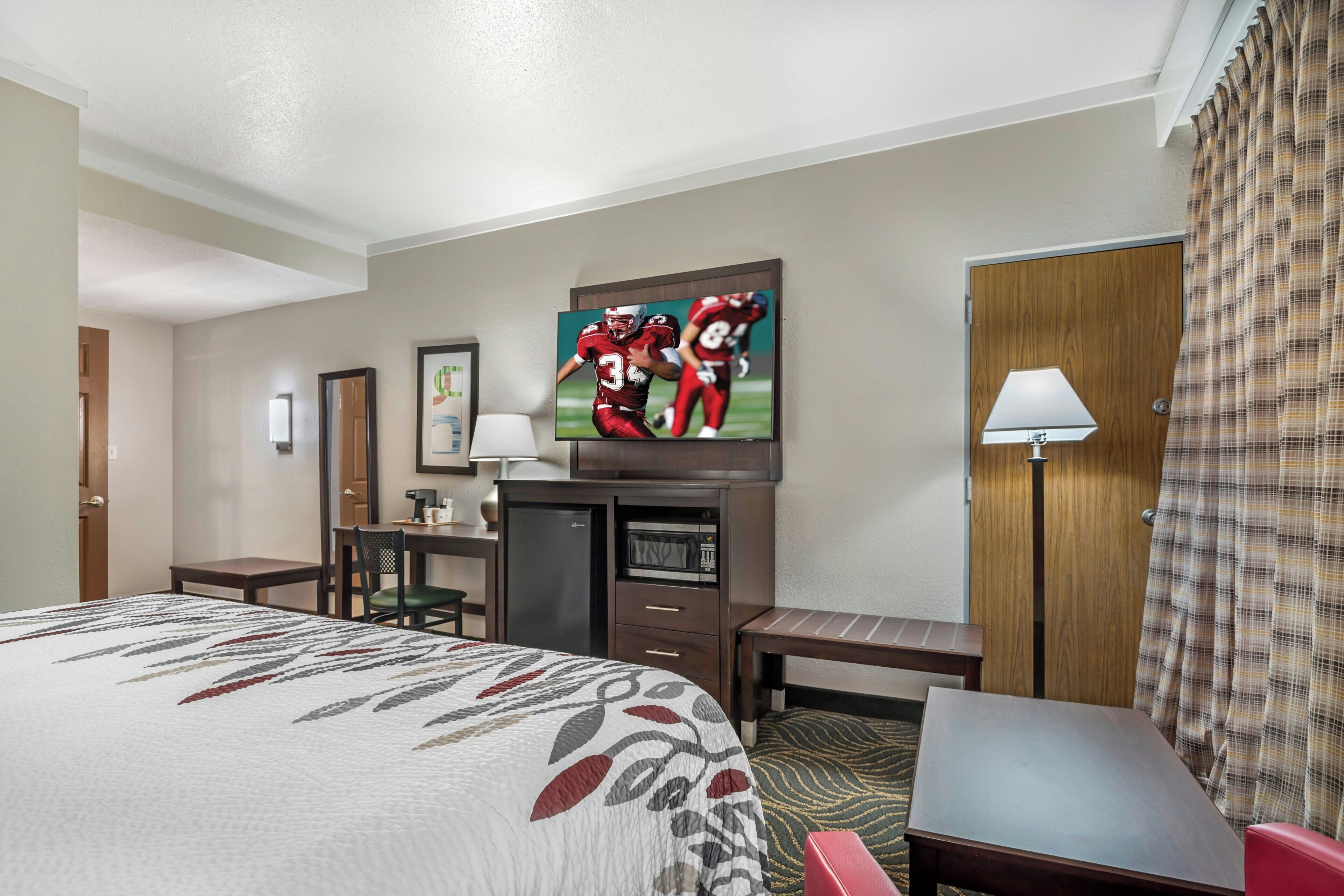 A hotel room with a bed, a desk, a television, a lamp, and a door.
