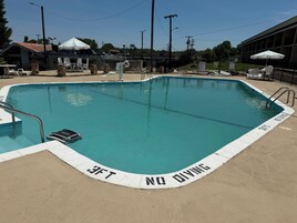 Una piscina con una torre de salvavidas, sillas de descanso y sombrillas.