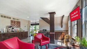 A modern hotel lobby with a kitchen area, red chairs, a large potted plant, and a sign indicating free Wi-Fi. - Red Roof Inn Gastonia (Gastonia)
