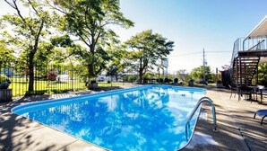 Ein rechteckiger Swimmingpool mit Metallleiter, umgeben von einer gepflasterten Liegefläche und einem Metallzaun.