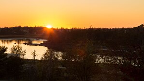 Ein Sonnenuntergang über einem See, im Vordergrund Bäume und eine entfernte Uferlinie.