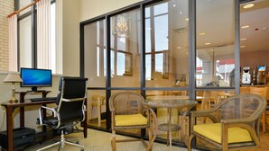 A modern office space with a computer desk, office chair, and two wicker chairs with yellow cushions.