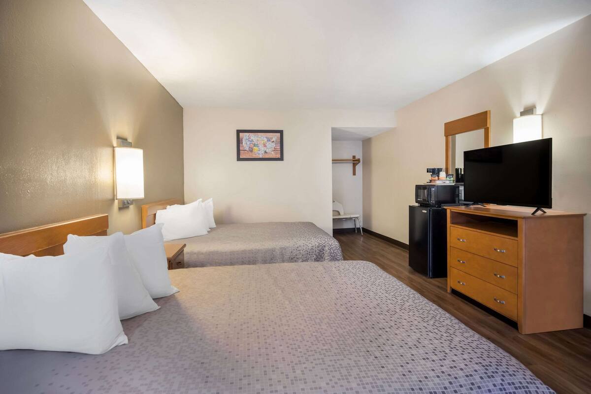 A hotel room with two beds, a TV, a dresser, and a small kitchenette.