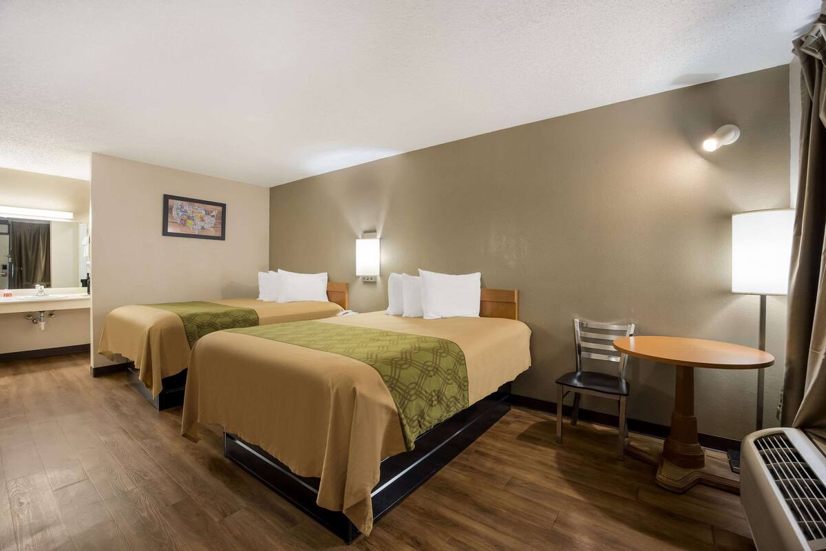 A hotel room with two beds, a small table, a chair, a lamp, and a mirror.