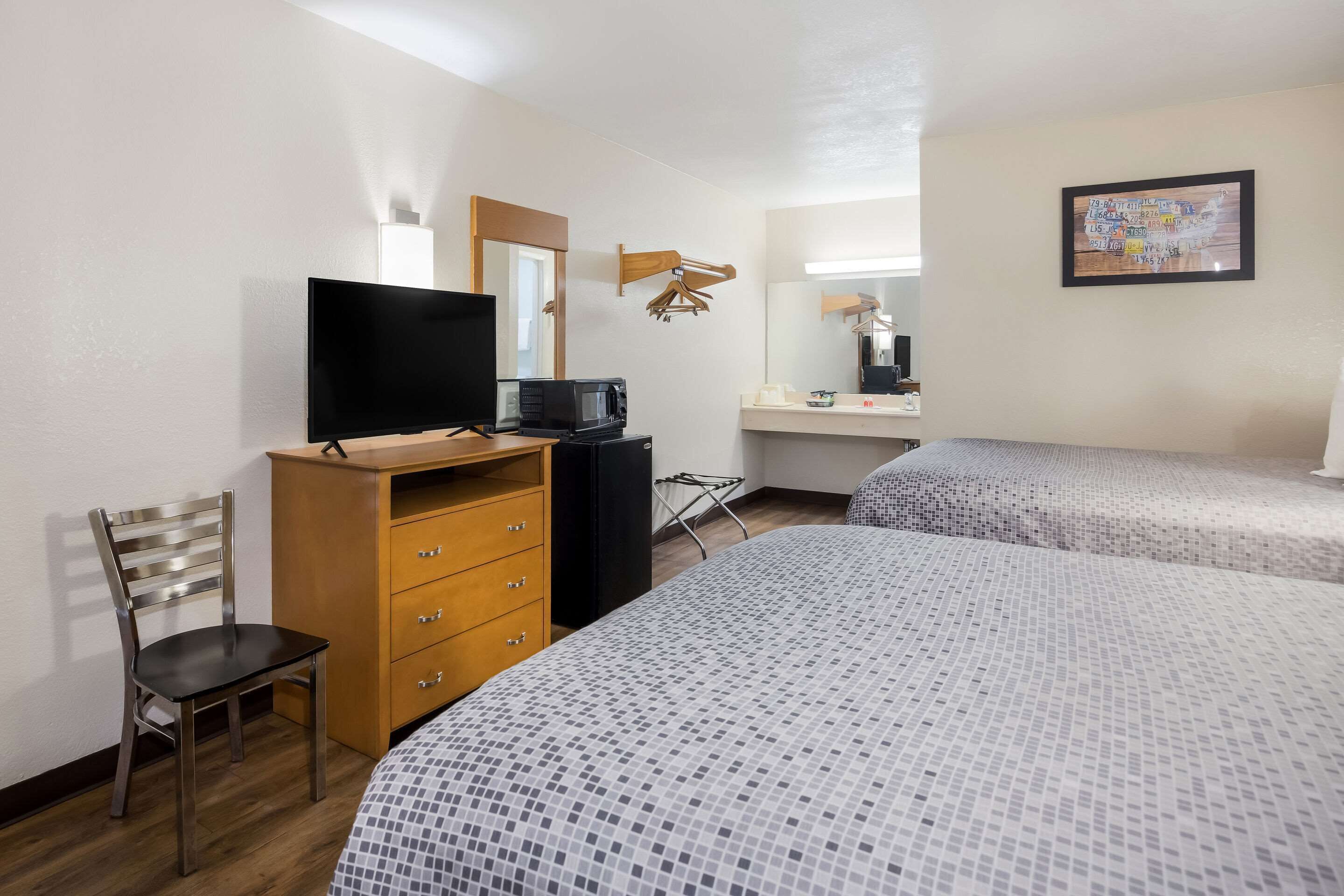 A hotel room with two beds, a TV, a wooden dresser, a chair, a microwave, and a mirror.