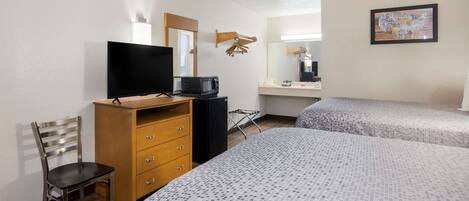 A hotel room with two beds, a TV, a wooden dresser, a chair, a microwave, and a mirror.
