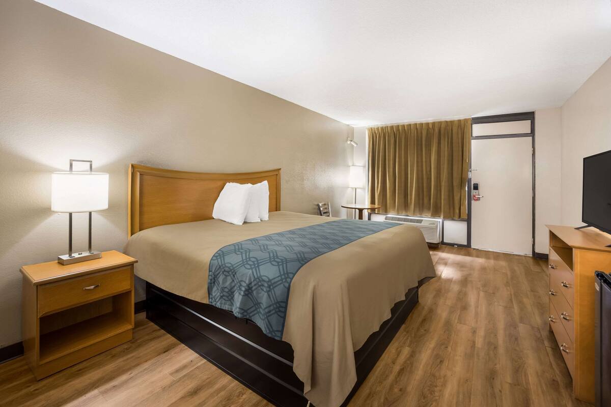 A hotel room with a bed, bedside tables, a television, a desk, and a window with curtains.