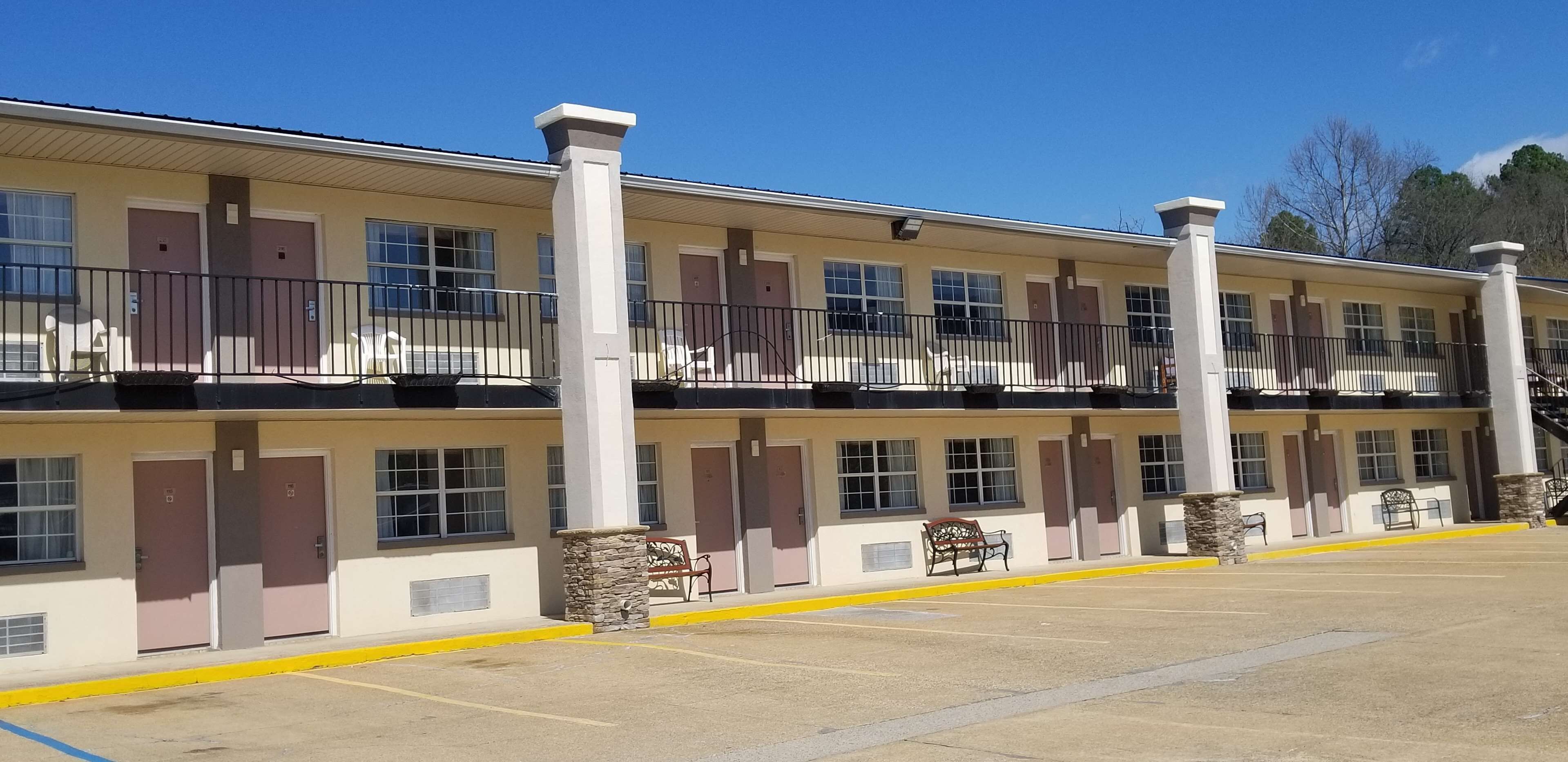 A multi-story motel with individual rooms, a parking lot, and a clear blue sky.