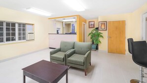 A waiting area with a reception desk, two armchairs, a table, and a potted plant. - Knights Inn Chattanooga (Chattanooga)