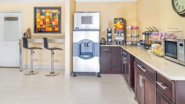A modern kitchen with a stainless steel refrigerator, a microwave, and a coffee machine. There are two bar stools and a clock on the wall. - Knights Inn Chattanooga (Chattanooga)