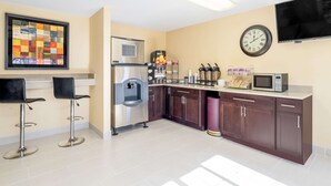 A modern kitchen with a stainless steel refrigerator, a microwave, and a water dispenser. There are two bar stools and a large clock on the wall. - Knights Inn Chattanooga (Chattanooga)