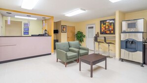 A reception area with a reception desk, two armchairs, a coffee table, a potted plant, a water dispenser, and a wall-mounted TV. - Knights Inn Chattanooga (Chattanooga)