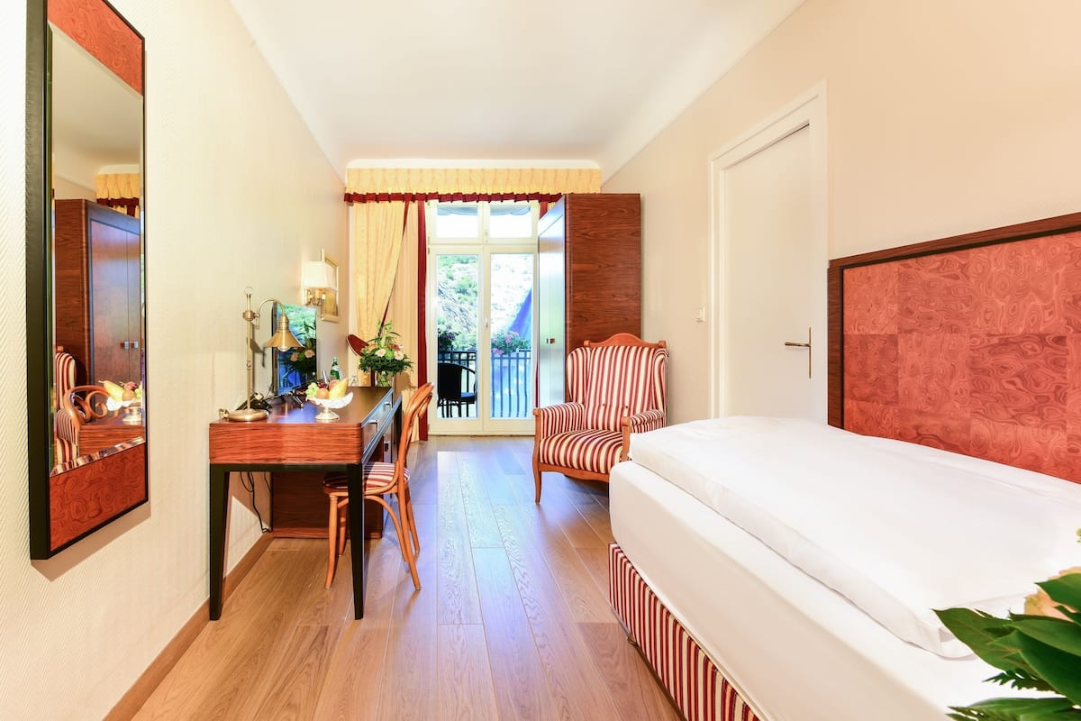 A hotel room with a wooden desk, a chair, a bed with a striped headboard, and a large mirror.