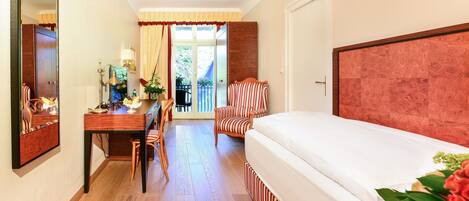 Une chambre d’hôtel avec un bureau en bois, une chaise, un lit doté d’une tête de lit à rayures et un grand miroir.