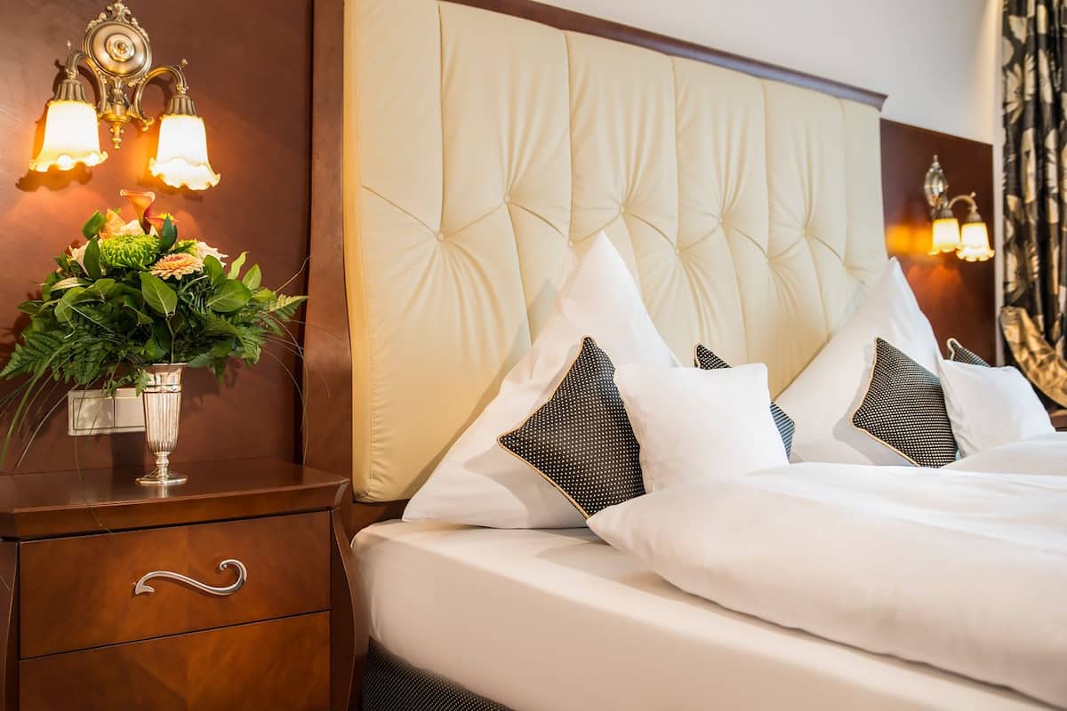 A hotel room with a tufted headboard, a bedside table with a vase of flowers, and two wall-mounted light fixtures.