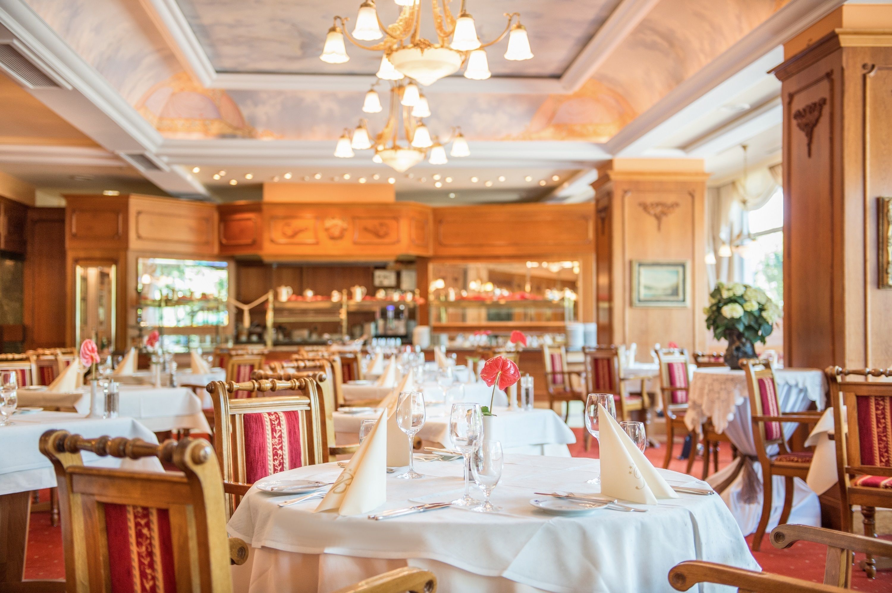 A restaurant with round tables, wooden chairs, and chandeliers.