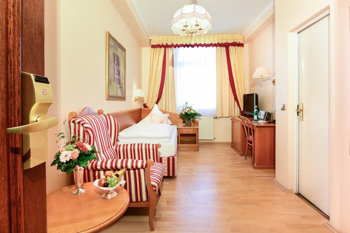 A hotel room with a bed, a sofa, a desk with a lamp, a TV, and a window with curtains.