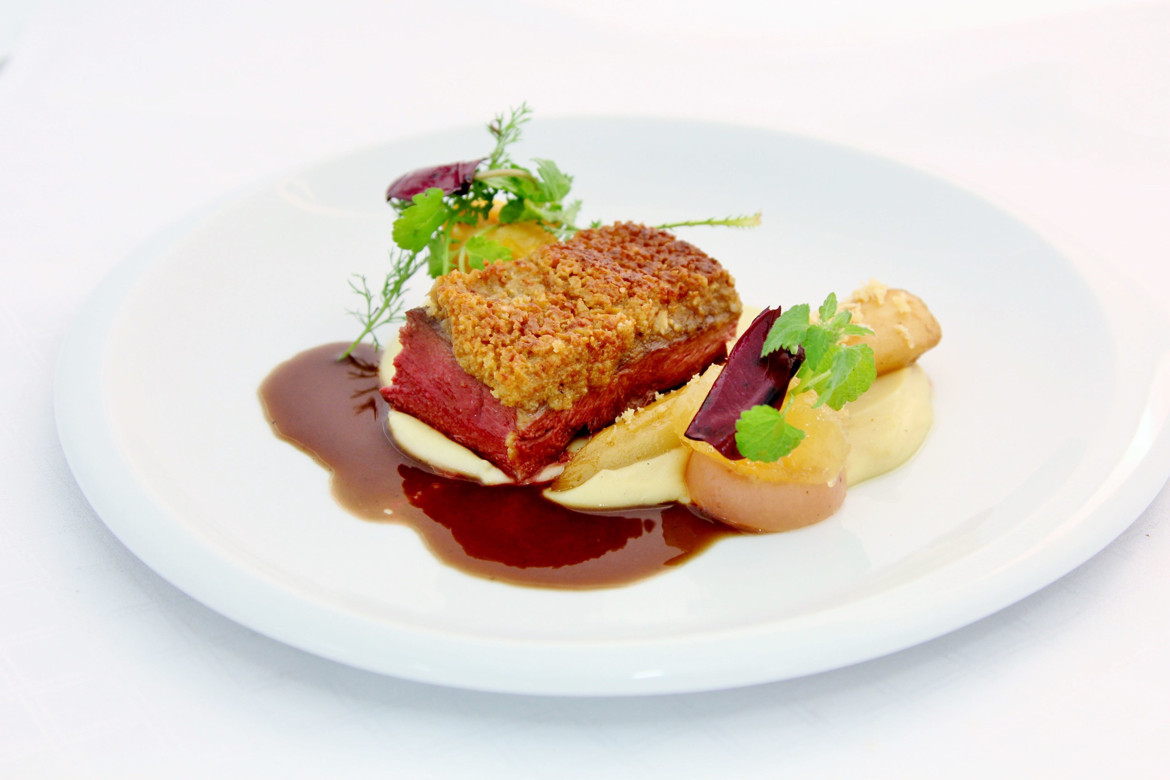 Une assiette blanche contenant un morceau de viande panée, une tranche de viande rouge et quelques légumes.