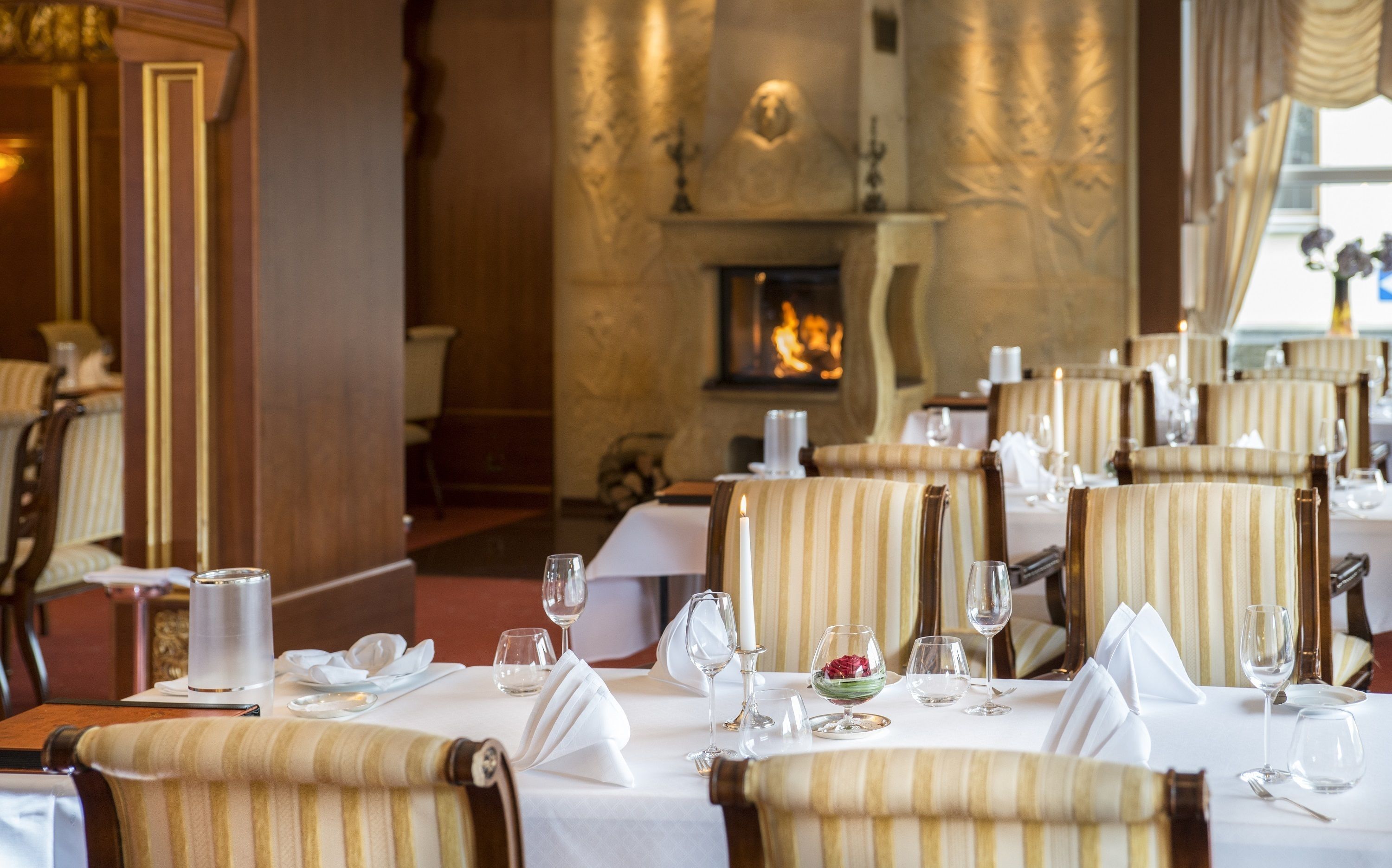 Ein Restaurant mit gedeckten Tischen, Stühlen mit Streifenbezug und einem Kamin im Hintergrund.