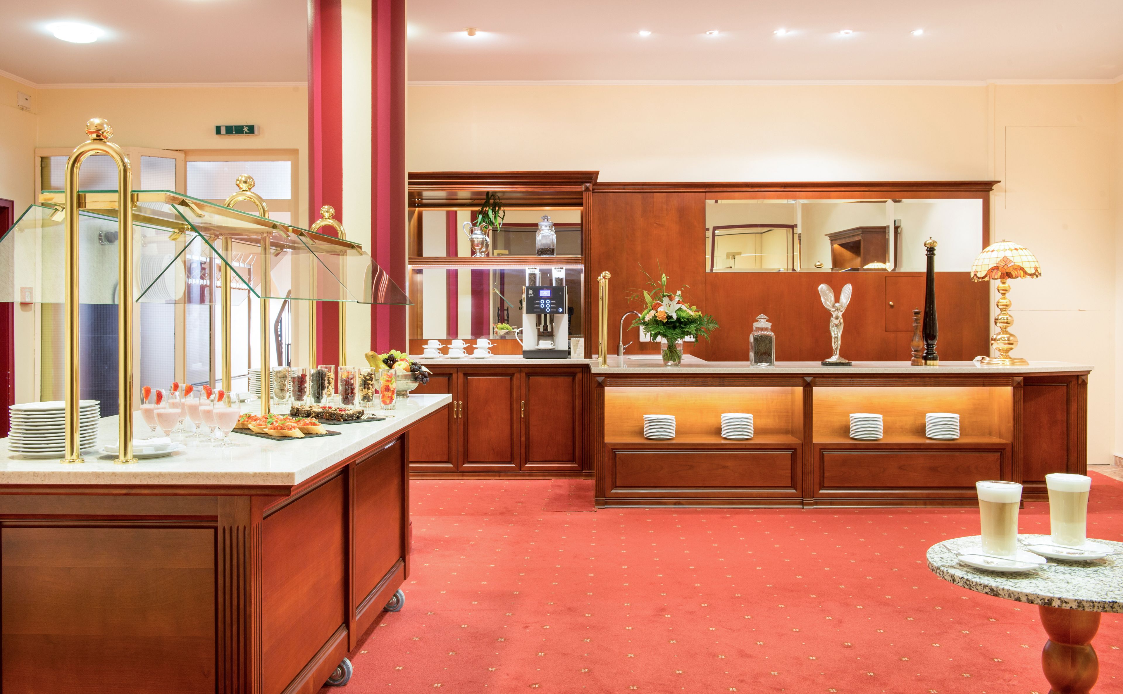 A hotel lobby with a reception desk, a coffee machine, and a buffet area with food and drinks.