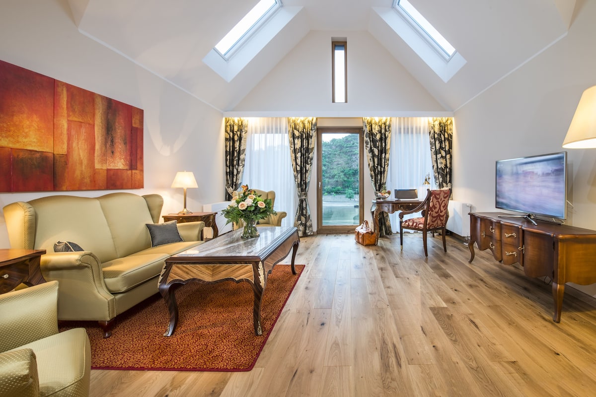 A spacious living room with a high ceiling, a large painting on the wall, a sofa, a coffee table, and a television.