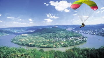 Een persoon paraglidet boven een rond eiland met een rivier en het omliggende landschap.