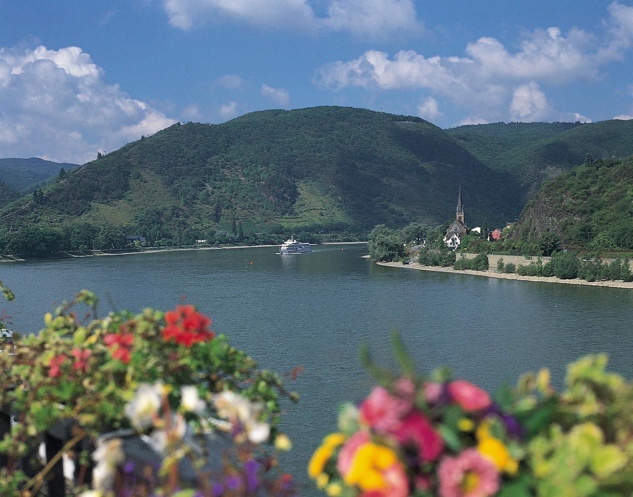Ein Fluss mit einem Boot, umgeben von grünen Hügeln und einer Kirche.