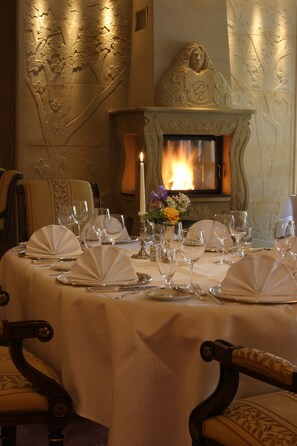 Enjoy a romantic meal in this elegant dining area with a beautifully set table, fireplace, and floral accents.