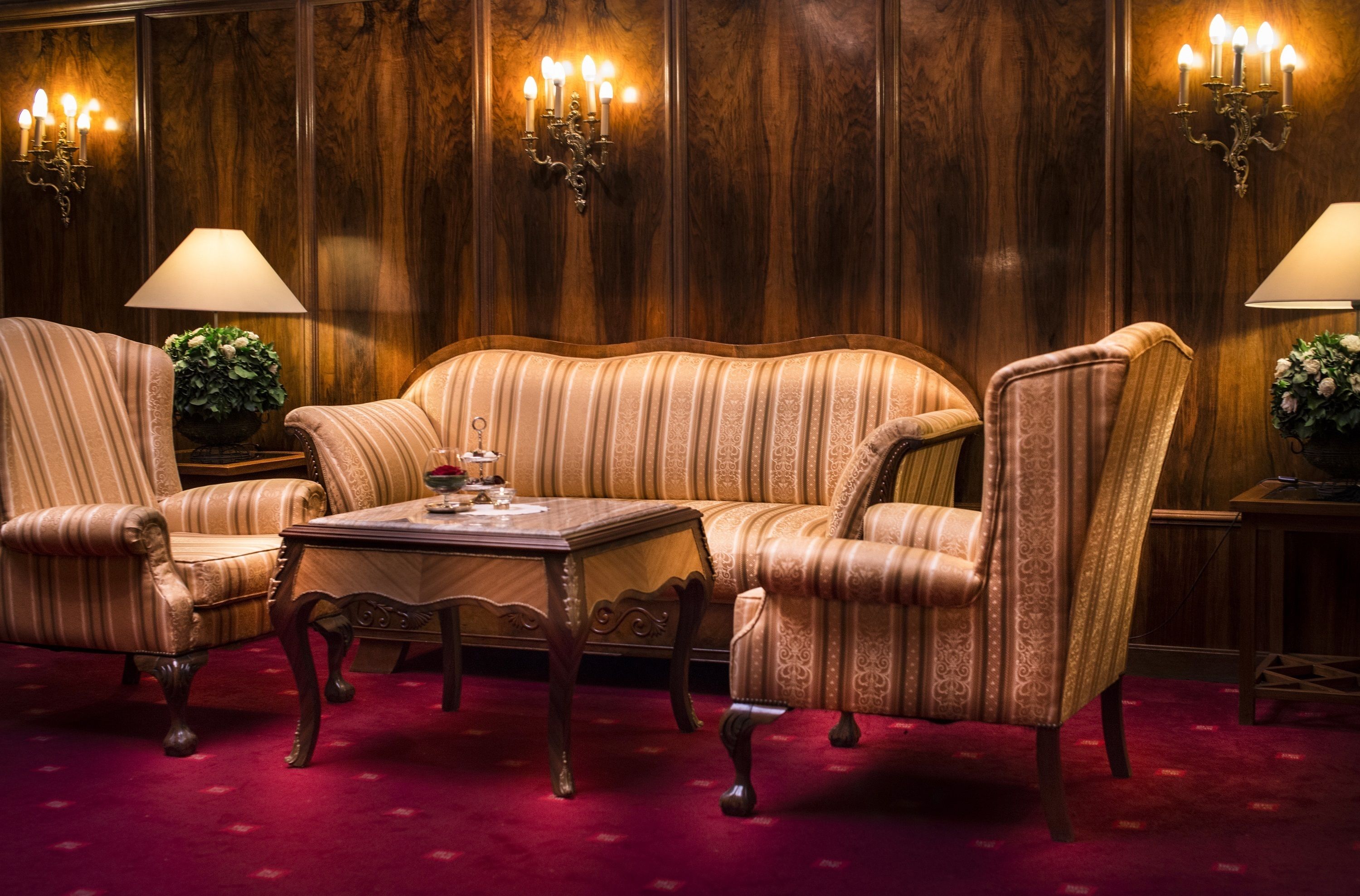 Una habitación con un sofá a rayas, dos sillones, una mesa de centro de madera y una alfombra roja.